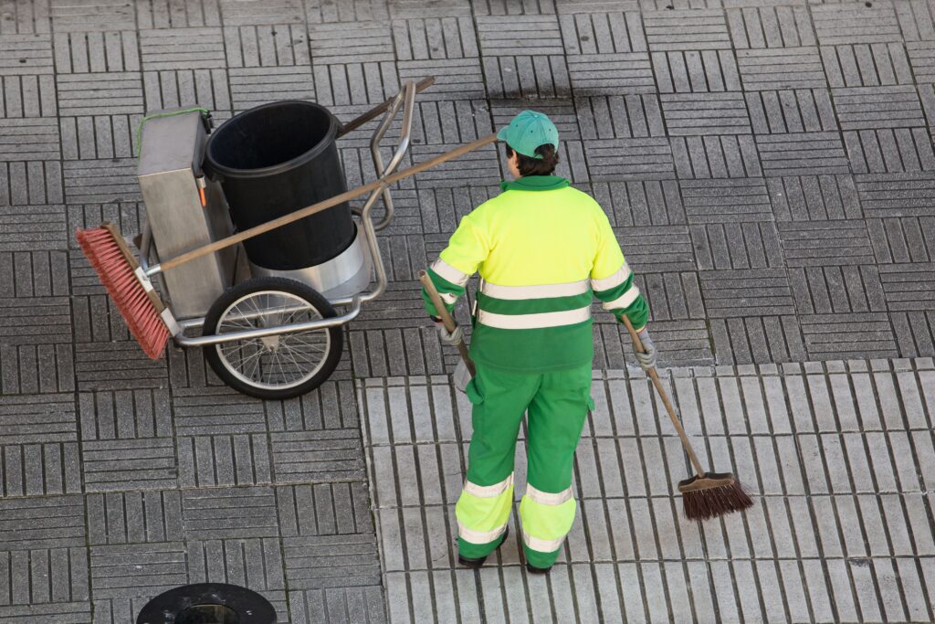 Street sweeper working on a sidewalk with her shovel, trolley and broom